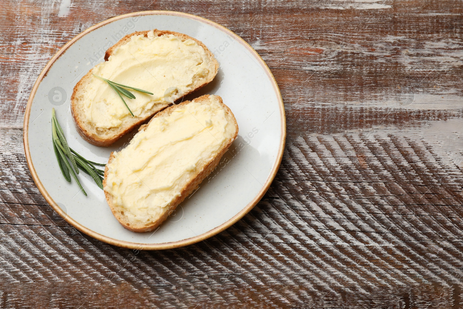 Fresh bread with butter and rosemary on wooden table, top view. Space for text Photo of Fresh bread with butter and rosemary on wooden table, top view. Space for text