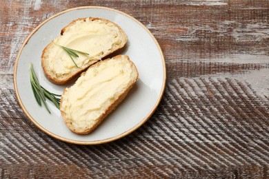 Photo of Fresh bread with butter and rosemary on wooden table, top view. Space for text