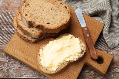 Photo of Fresh bread with butter and knife on wooden table, above view