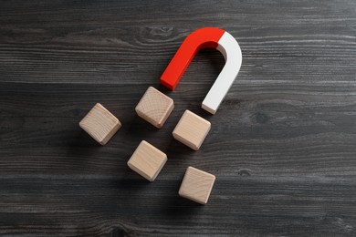 Magnet attracting cubes on wooden table, flat lay