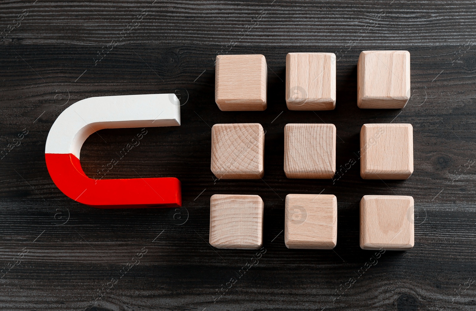 Photo of Magnet attracting cubes on wooden table, flat lay