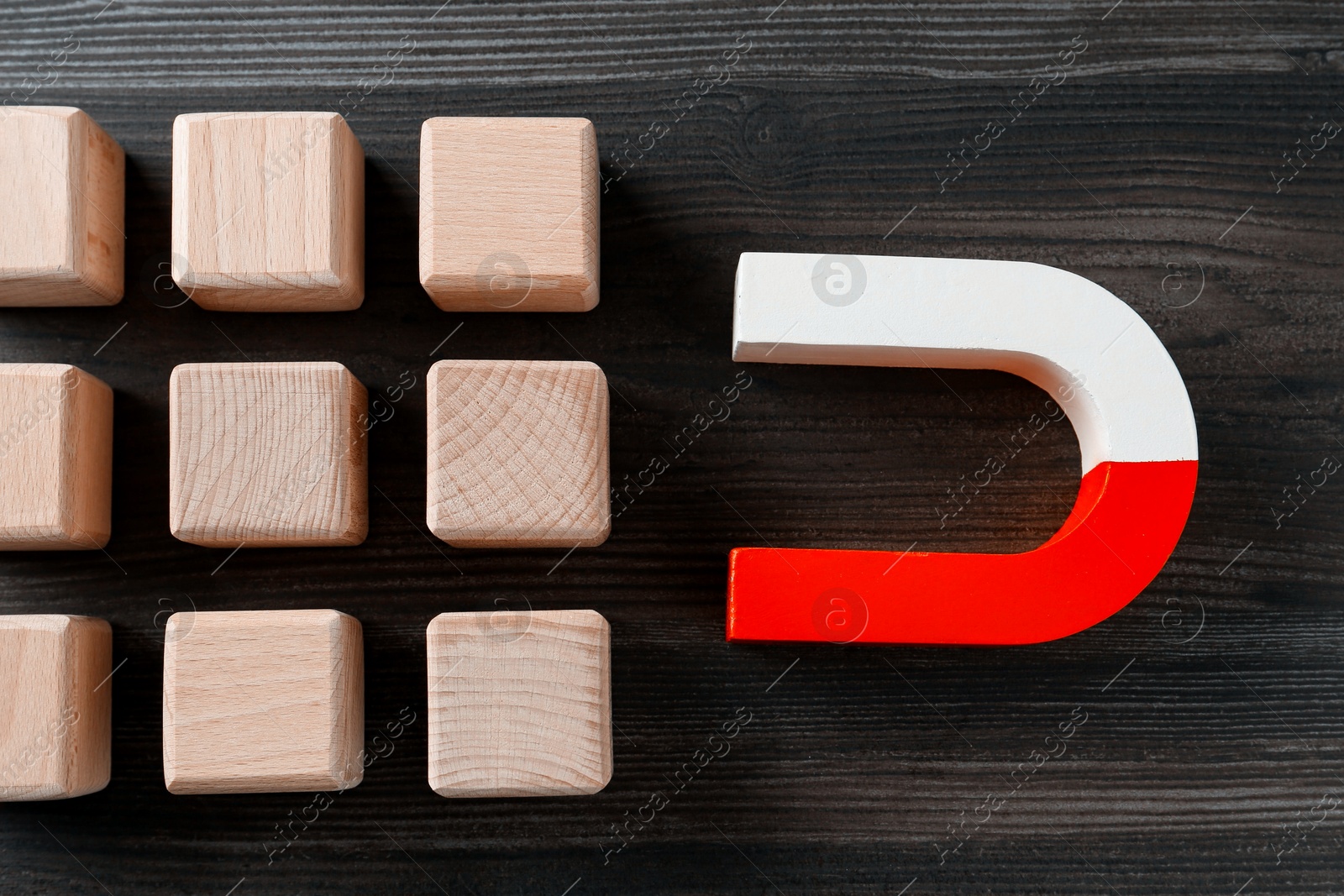 Photo of Magnet attracting cubes on wooden table, flat lay