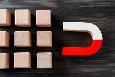 Photo of Magnet attracting cubes on wooden table, flat lay