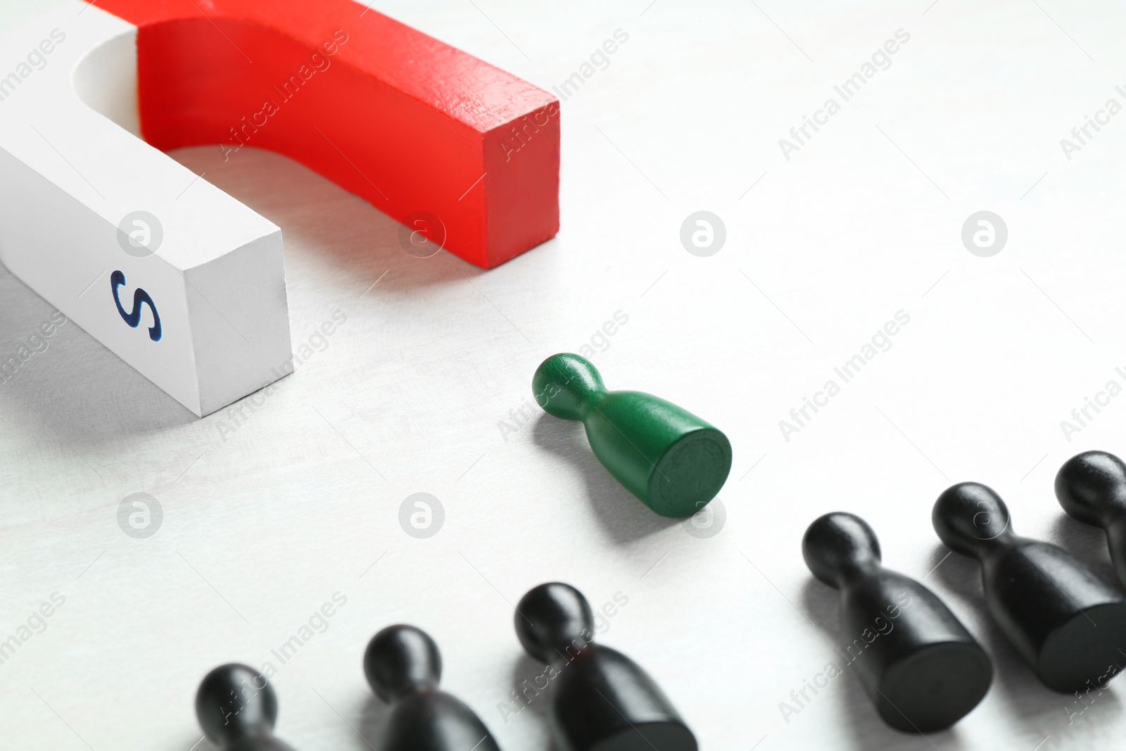 Photo of Magnet attracting green game piece among black ones on white table, closeup