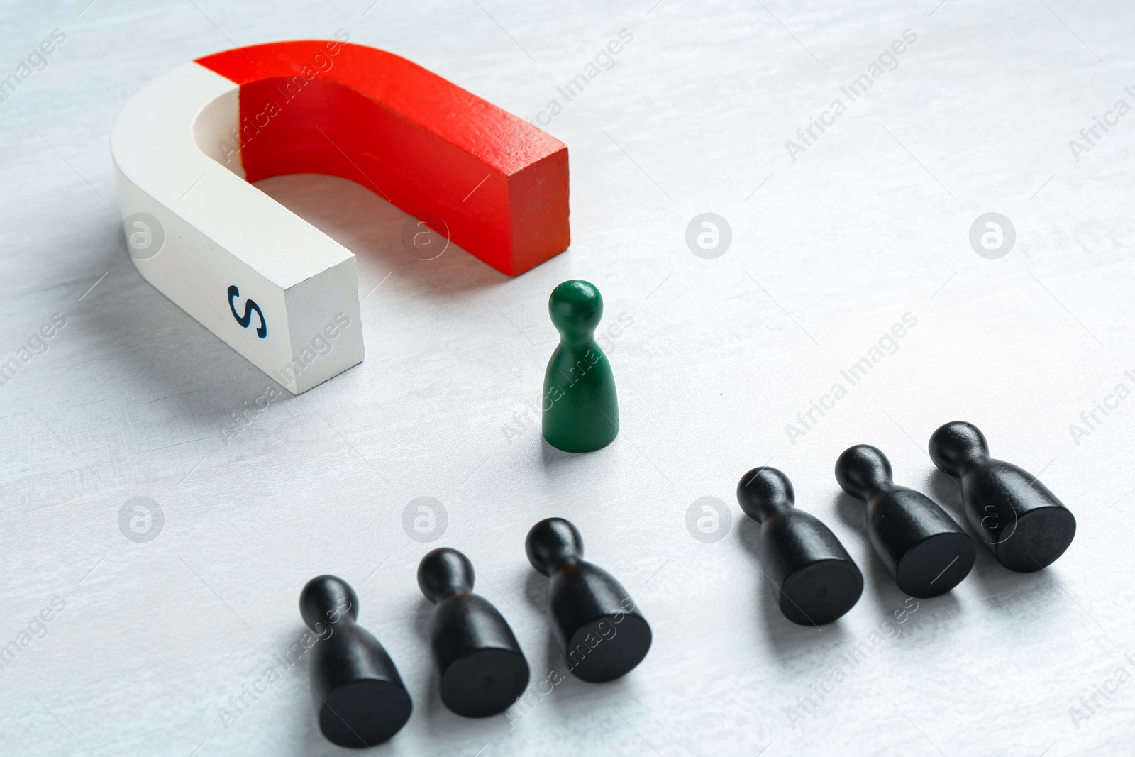 Photo of Magnet attracting green game piece among black ones on white table, closeup