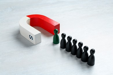 Photo of Magnet attracting green game piece among black ones on white table, closeup