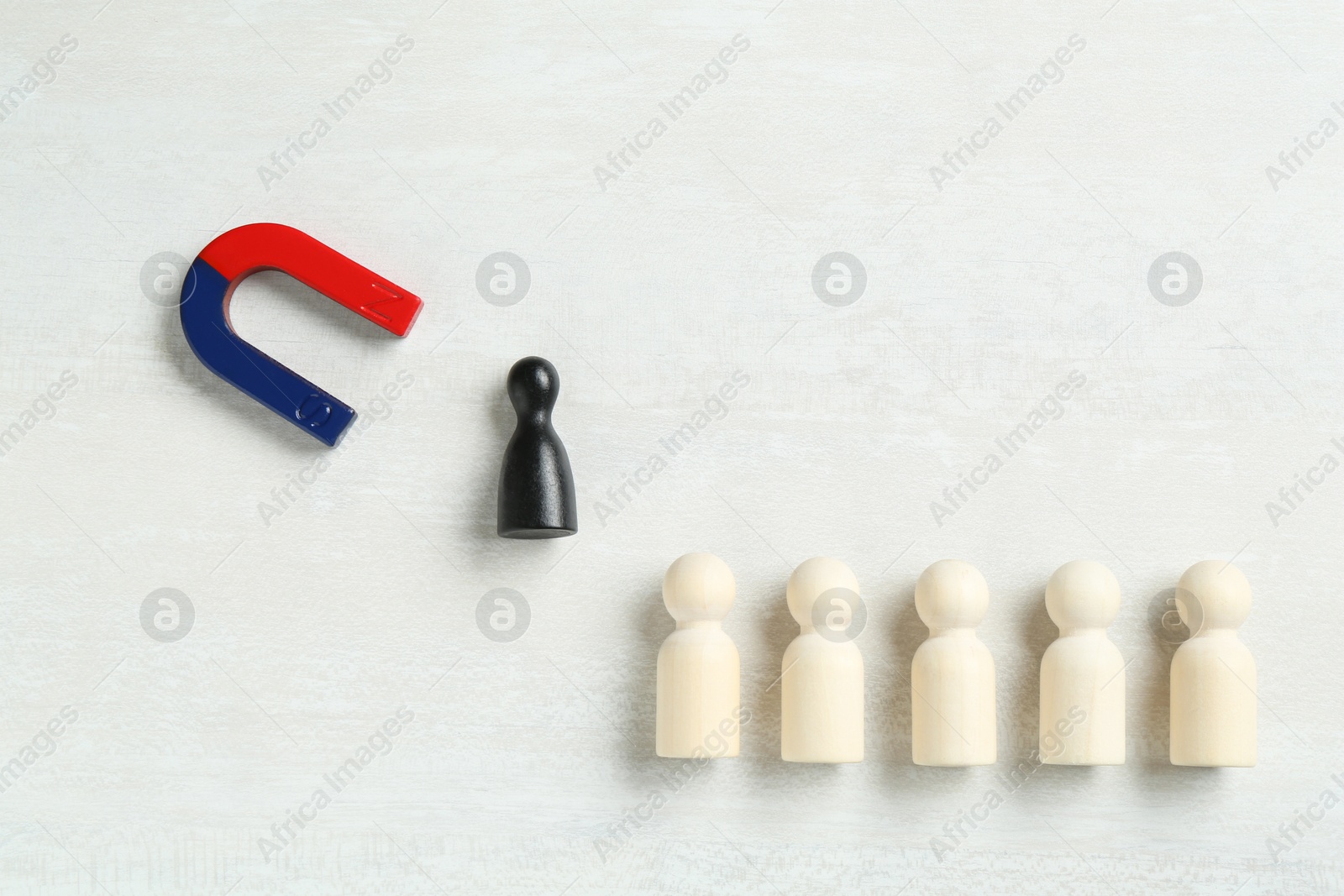 Photo of Magnet attracting black game piece among wooden ones on white table, flat lay