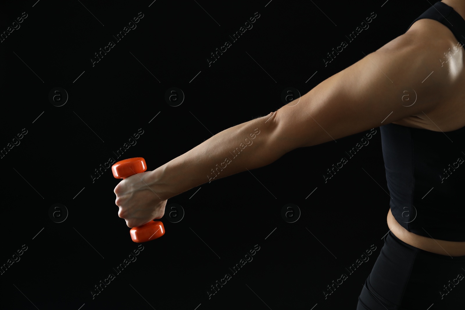 Photo of Woman exercising with dumbbell on black background, closeup