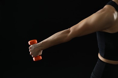 Photo of Woman exercising with dumbbell on black background, closeup