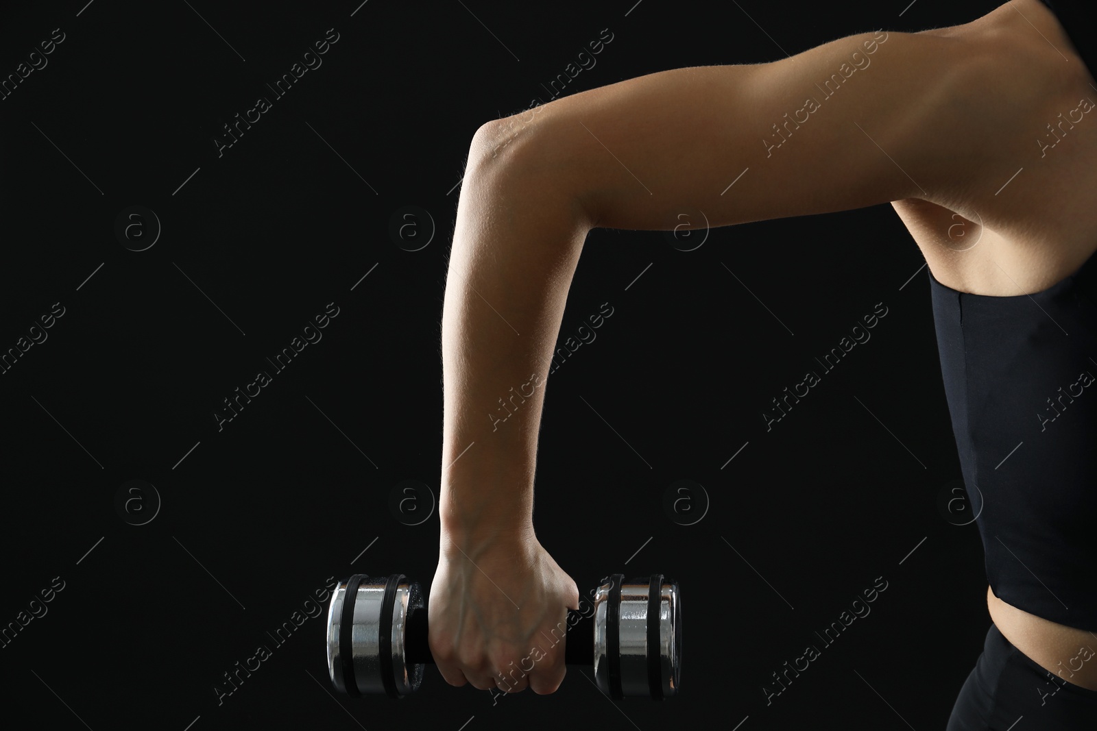 Photo of Woman exercising with dumbbell on black background, closeup