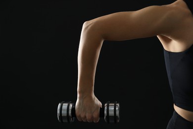 Photo of Woman exercising with dumbbell on black background, closeup