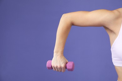 Photo of Woman exercising with dumbbell on purple background, closeup. Space for text