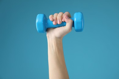 Photo of Woman exercising with dumbbell on light blue background, closeup