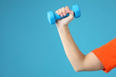 Photo of Woman exercising with dumbbell on light blue background, closeup. Space for text