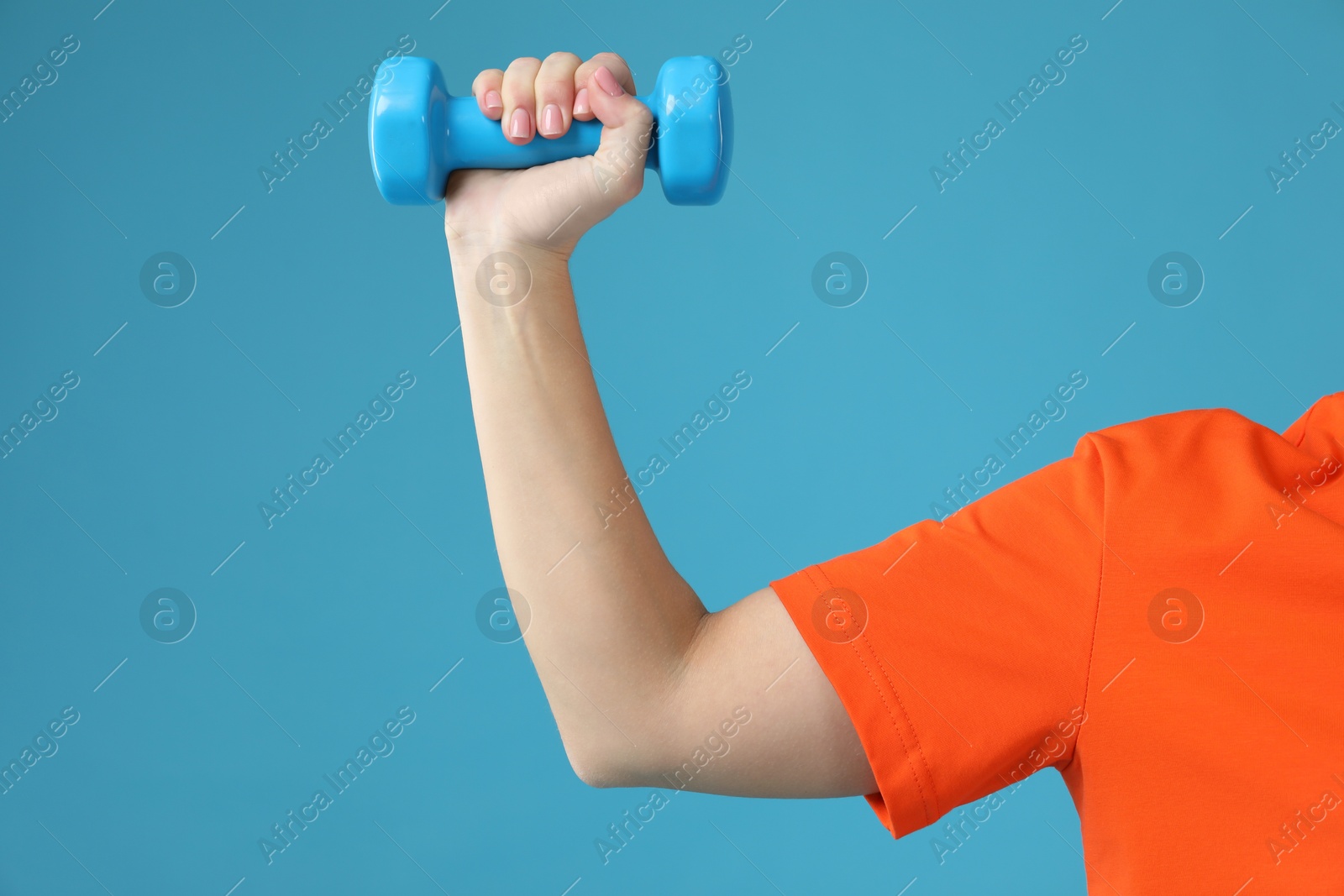 Photo of Woman exercising with dumbbell on light blue background, closeup