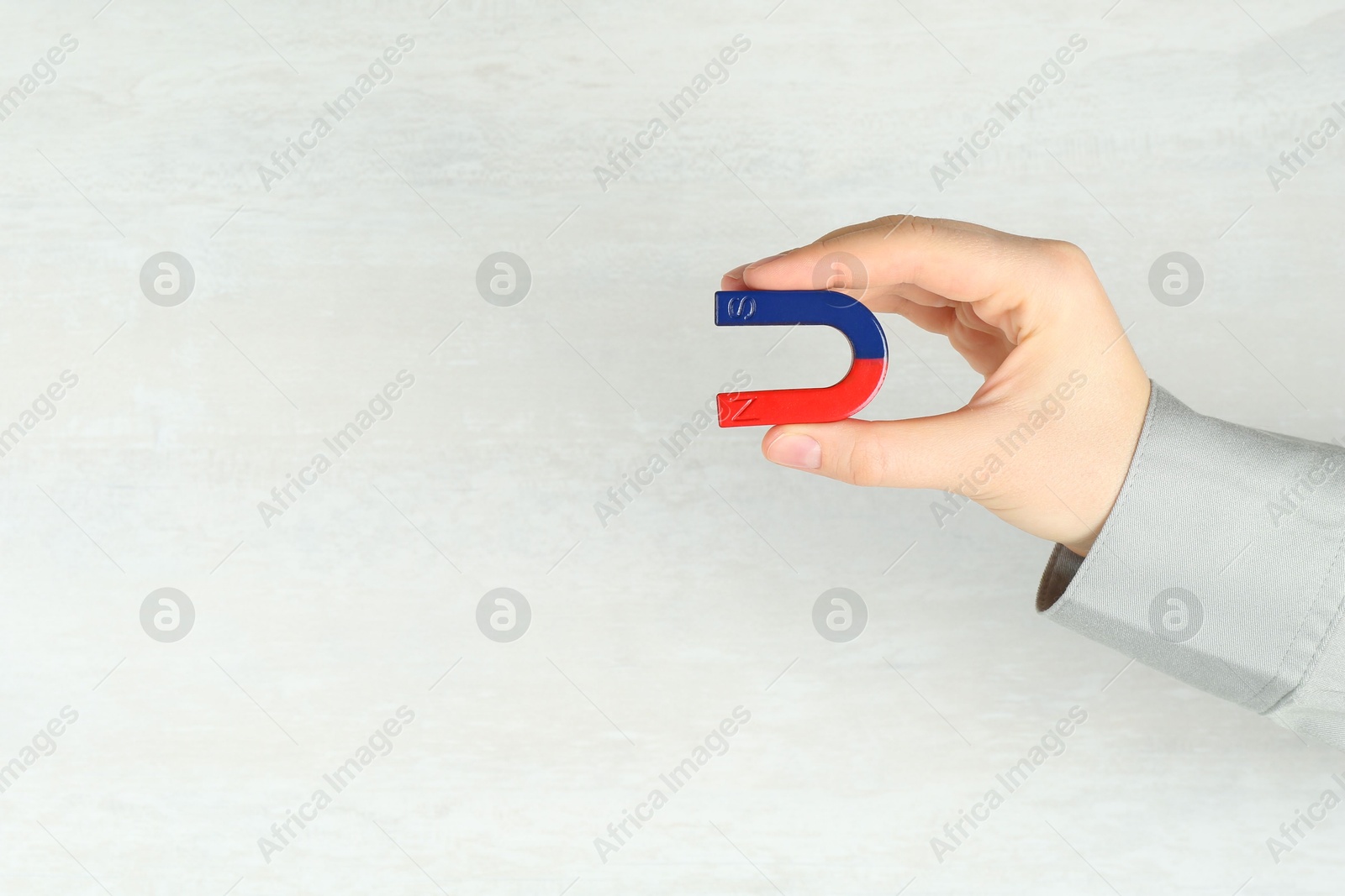 Photo of Woman with horseshoe magnet on light background, closeup. Space for text