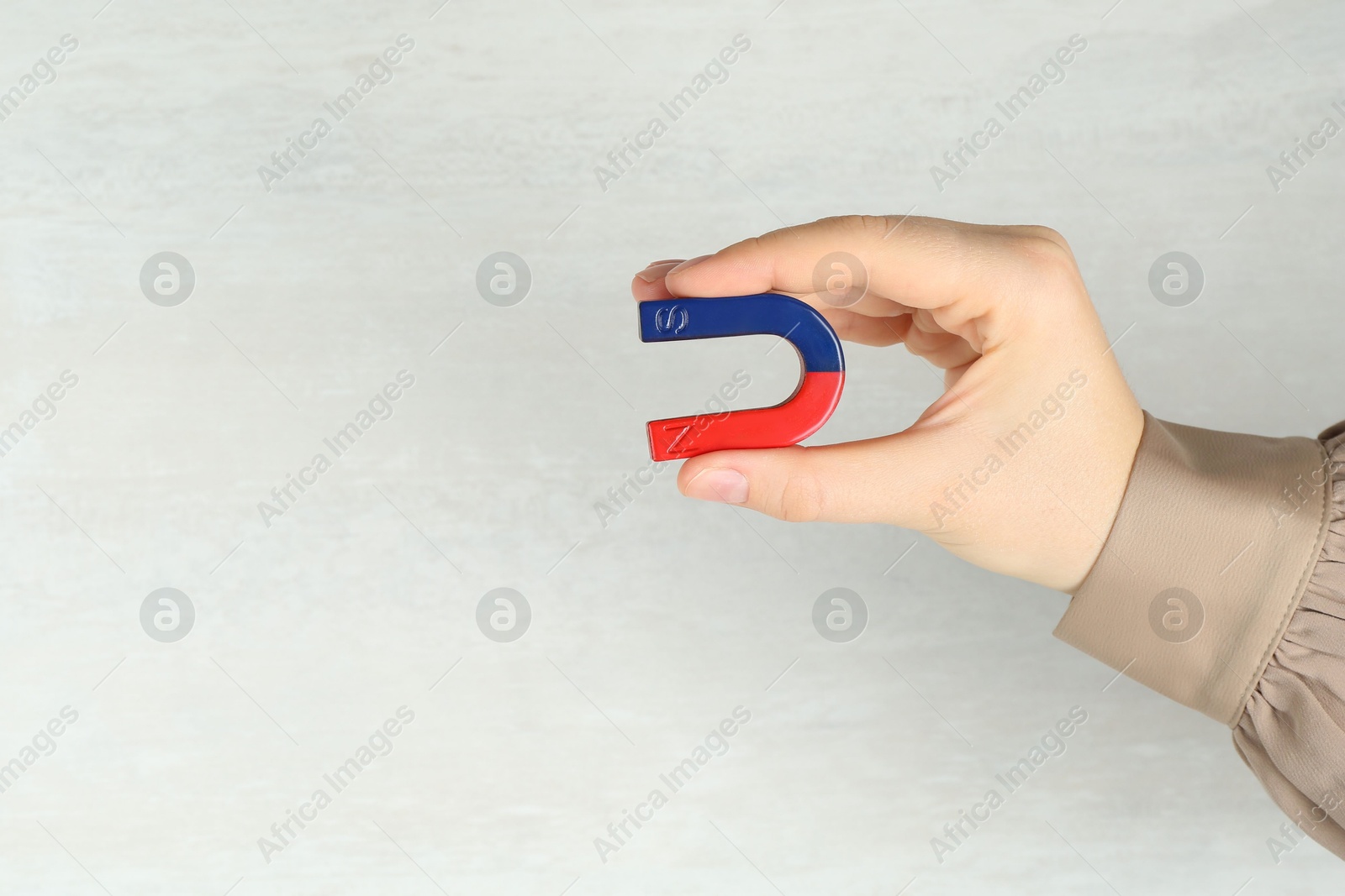 Photo of Woman with horseshoe magnet on light background, closeup. Space for text