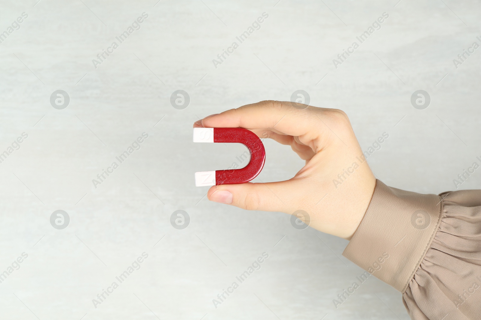 Photo of Woman with horseshoe magnet on light background, closeup