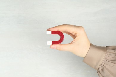 Photo of Woman with horseshoe magnet on light background, closeup