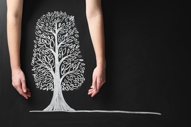 Photo of Woman keeping safe tree drawn on chalkboard, closeup. Space for text