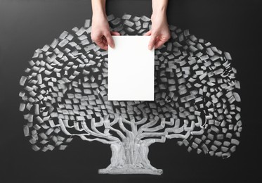 Photo of Woman holding blank paper sheet over chalkboard with tree drawing, closeup