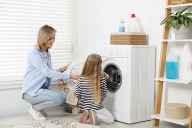 Photo of Little girl helping her mom doing laundry at home