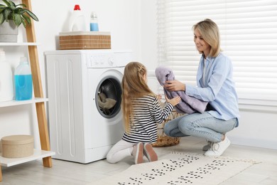 Photo of Little girl helping her mom doing laundry at home