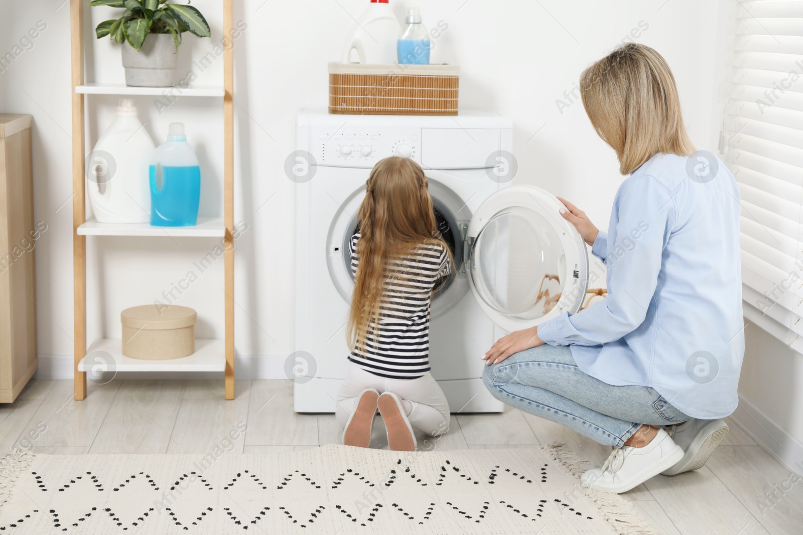 Photo of Little girl helping her mom doing laundry at home