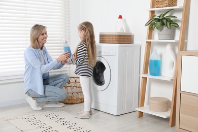 Photo of Little girl with detergent helping her mom doing laundry at home