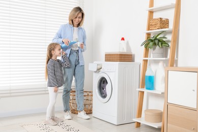 Photo of Little girl helping her mom doing laundry at home