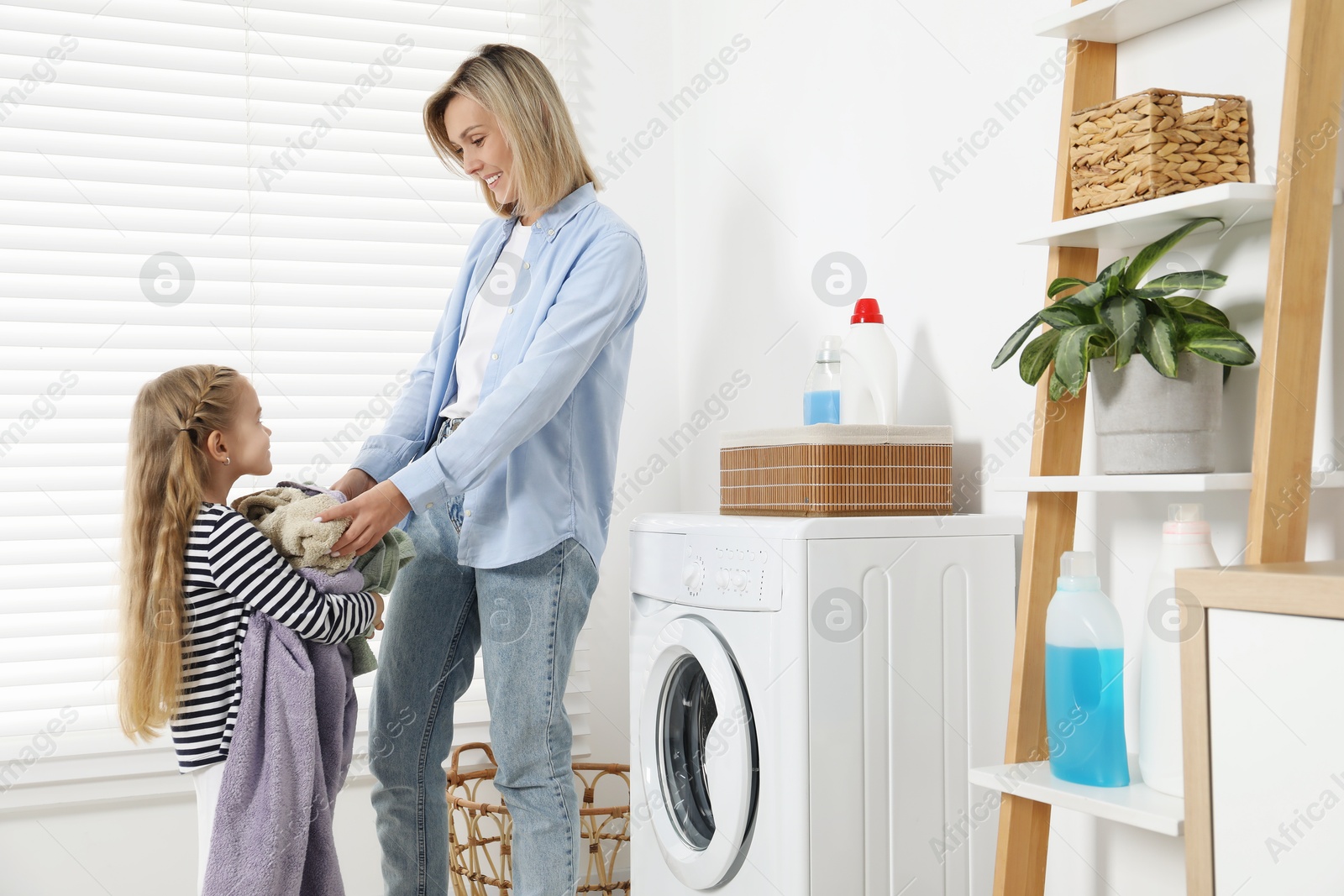 Photo of Little girl helping her mom doing laundry at home