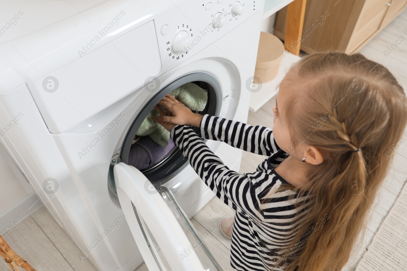 Photo of Little helper. Cute girl doing laundry at home, above view