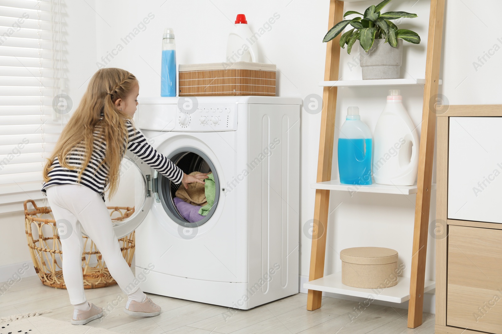 Photo of Little helper. Cute girl doing laundry at home, back view