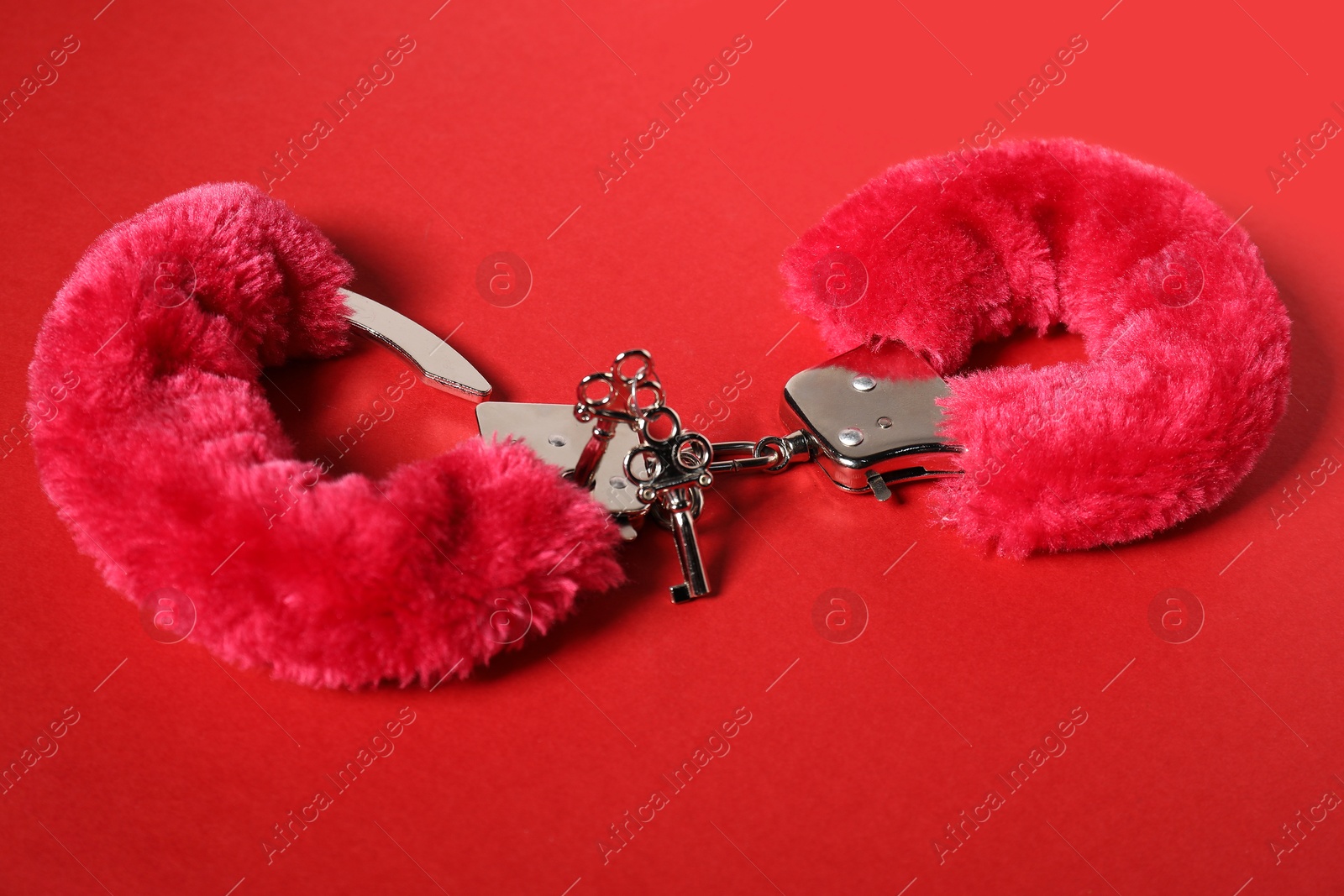 Photo of Bright fluffy handcuffs and keys on red background. Sex toy