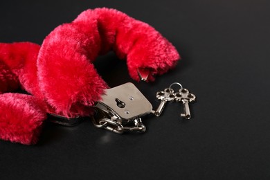 Photo of Bright fluffy handcuffs and keys on black background, space for text