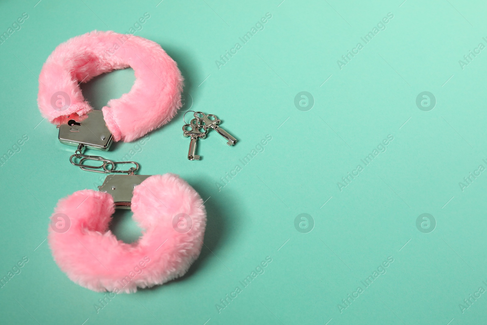 Photo of Bright fluffy handcuffs and keys on turquoise background. Space for text