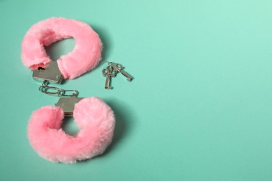 Photo of Bright fluffy handcuffs and keys on turquoise background. Space for text