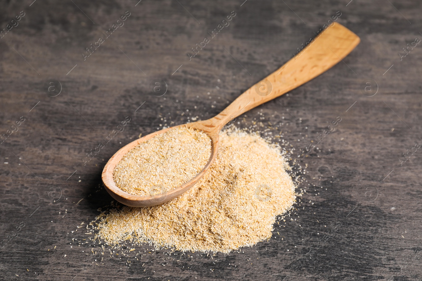 Photo of Oat bran in wooden spoon on grey table, closeup