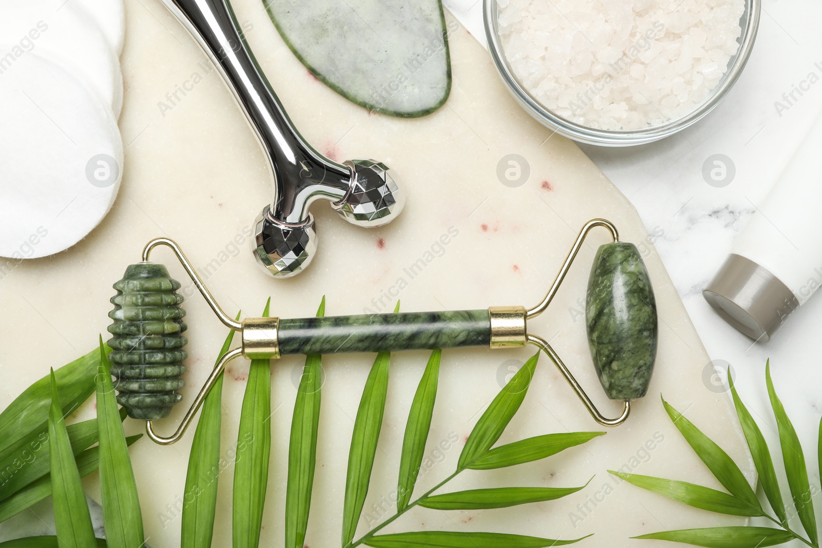 Photo of Flat lay composition with face rollers and gua sha tool on white marble background,