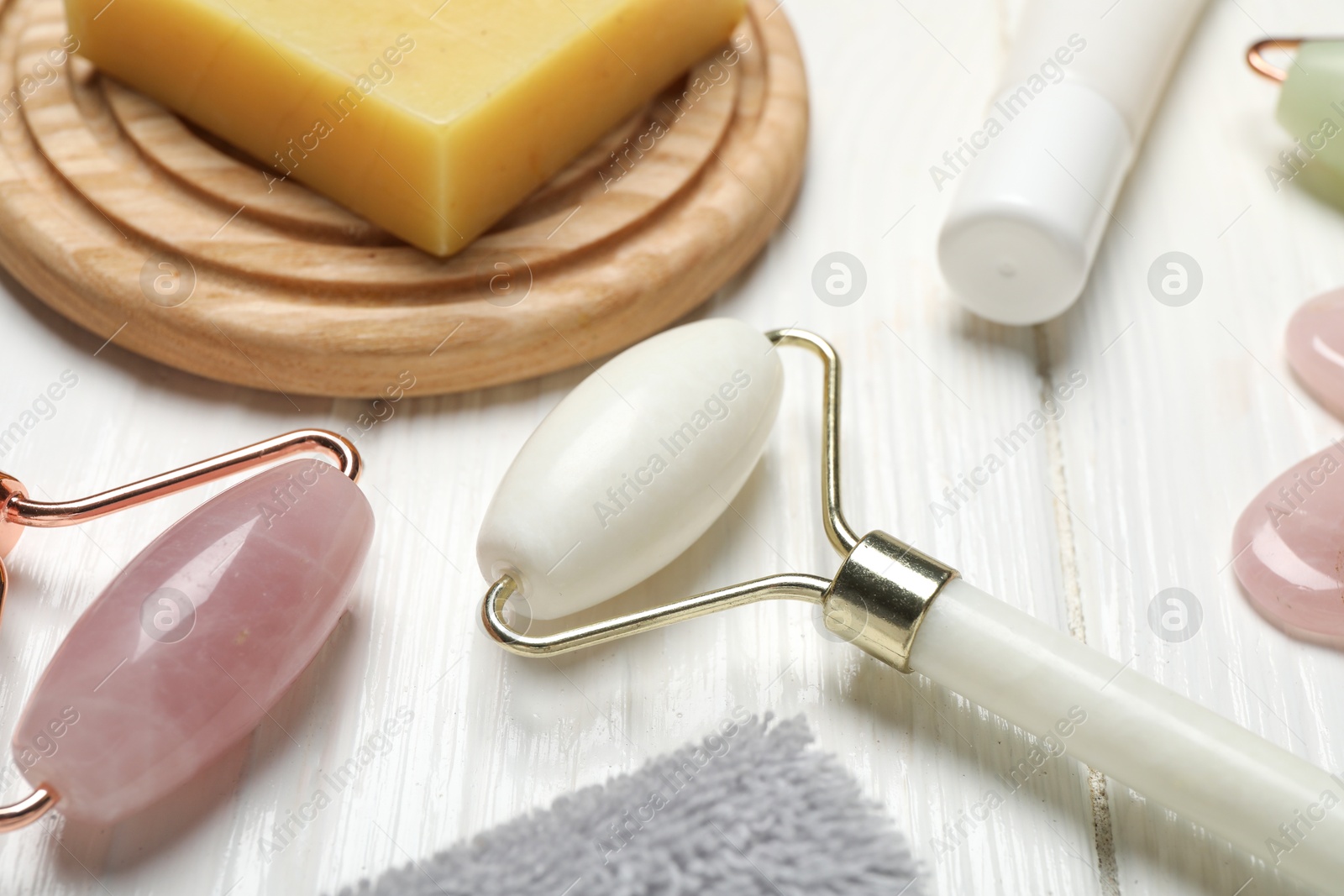 Photo of Face rollers, soap bar and cosmetic product on white wooden background, closeup