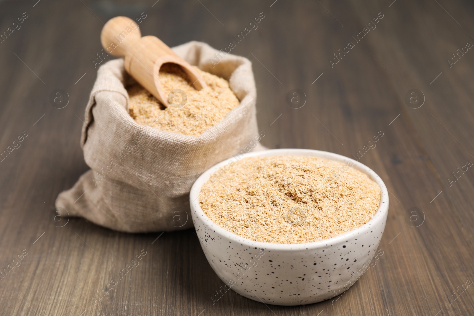 Photo of Oat bran in bowl, scoop and burlap bag on wooden table, closeup