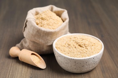 Photo of Oat bran in bowl, scoop and burlap bag on wooden table, closeup