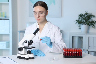 Photo of Laboratory testing. Doctor dripping blood sample onto glass slide while working with microscope at table indoors