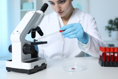 Photo of Laboratory testing. Doctor dripping blood sample onto glass slide while working with microscope at table indoors, selective focus