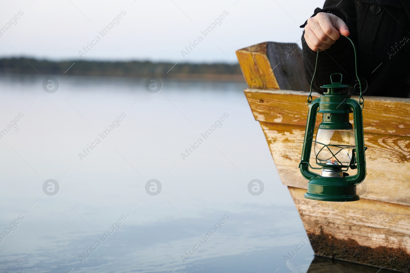 Photo of Man with vintage kerosene lamp near river in evening, closeup. Space for text