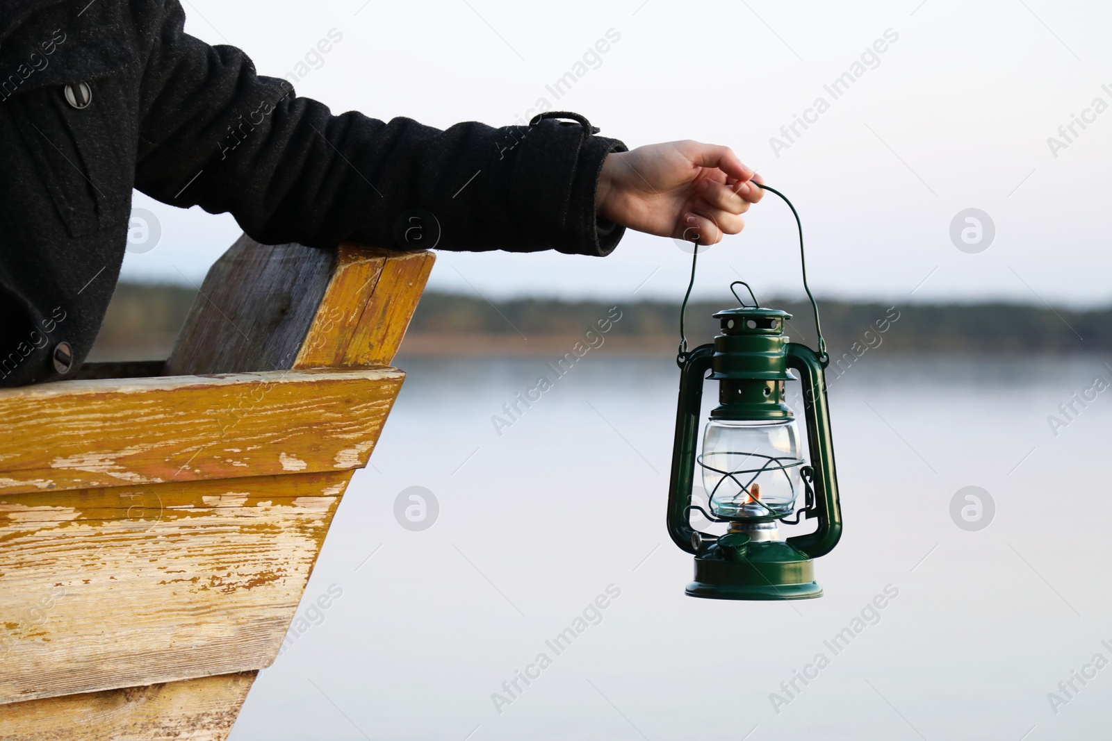 Photo of Man with vintage kerosene lamp near river in evening, closeup