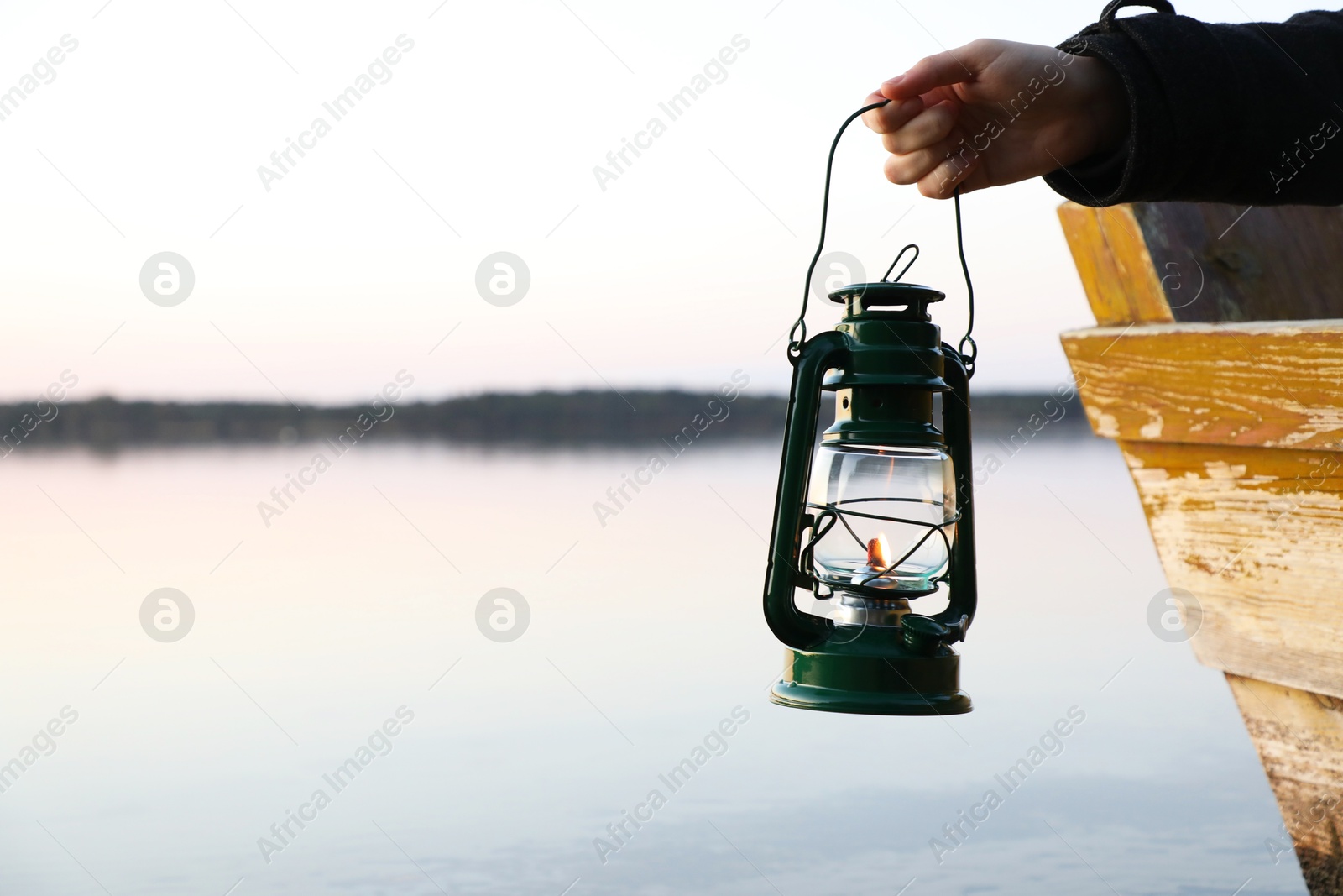 Photo of Man with vintage kerosene lamp near river in evening, closeup. Space for text