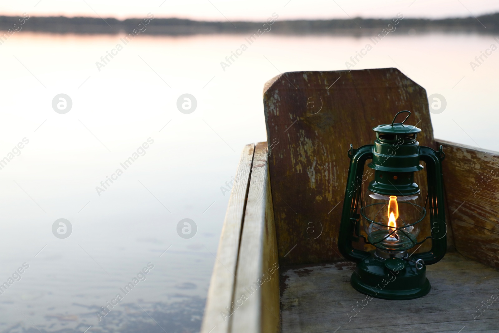 Photo of Vintage kerosene lamp in wooden boat near river at sunset