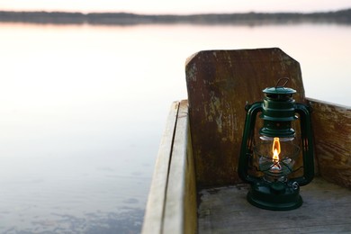 Photo of Vintage kerosene lamp in wooden boat near river at sunset