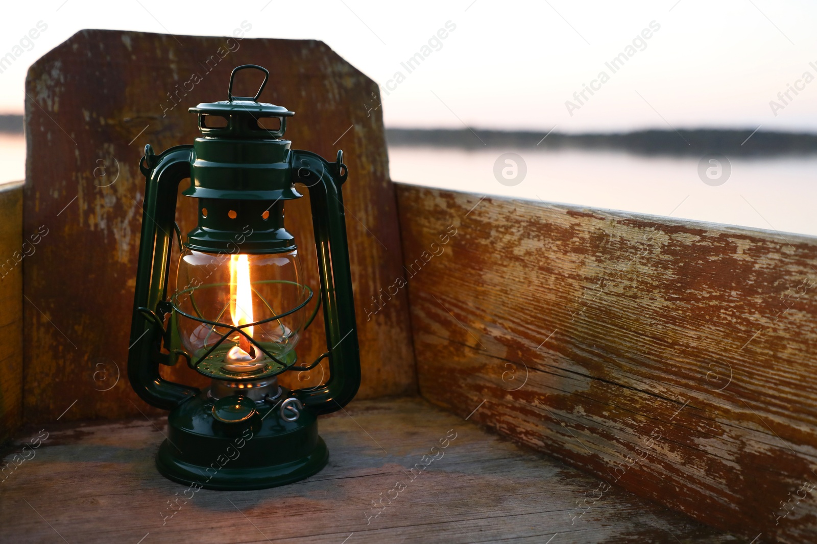 Photo of Vintage kerosene lamp in wooden boat near river at sunset